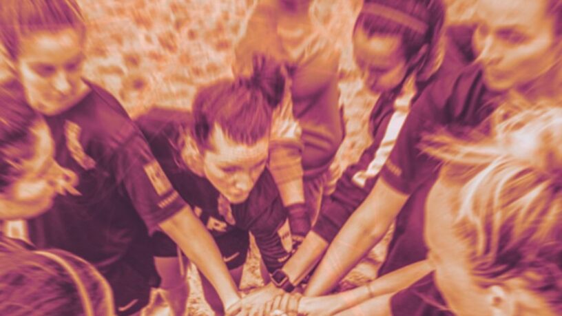 duotone image of women beach soccer players in a huddle